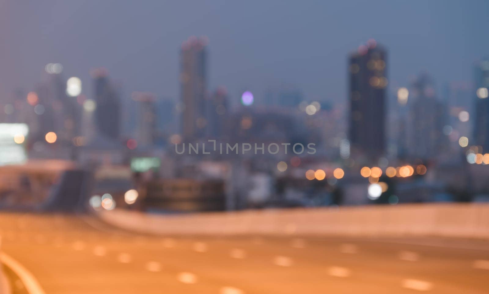 Abstract blurred cityscape at twilight with tall skyscrapers against hazy sky. City building lights twinkle in urban atmosphere background.