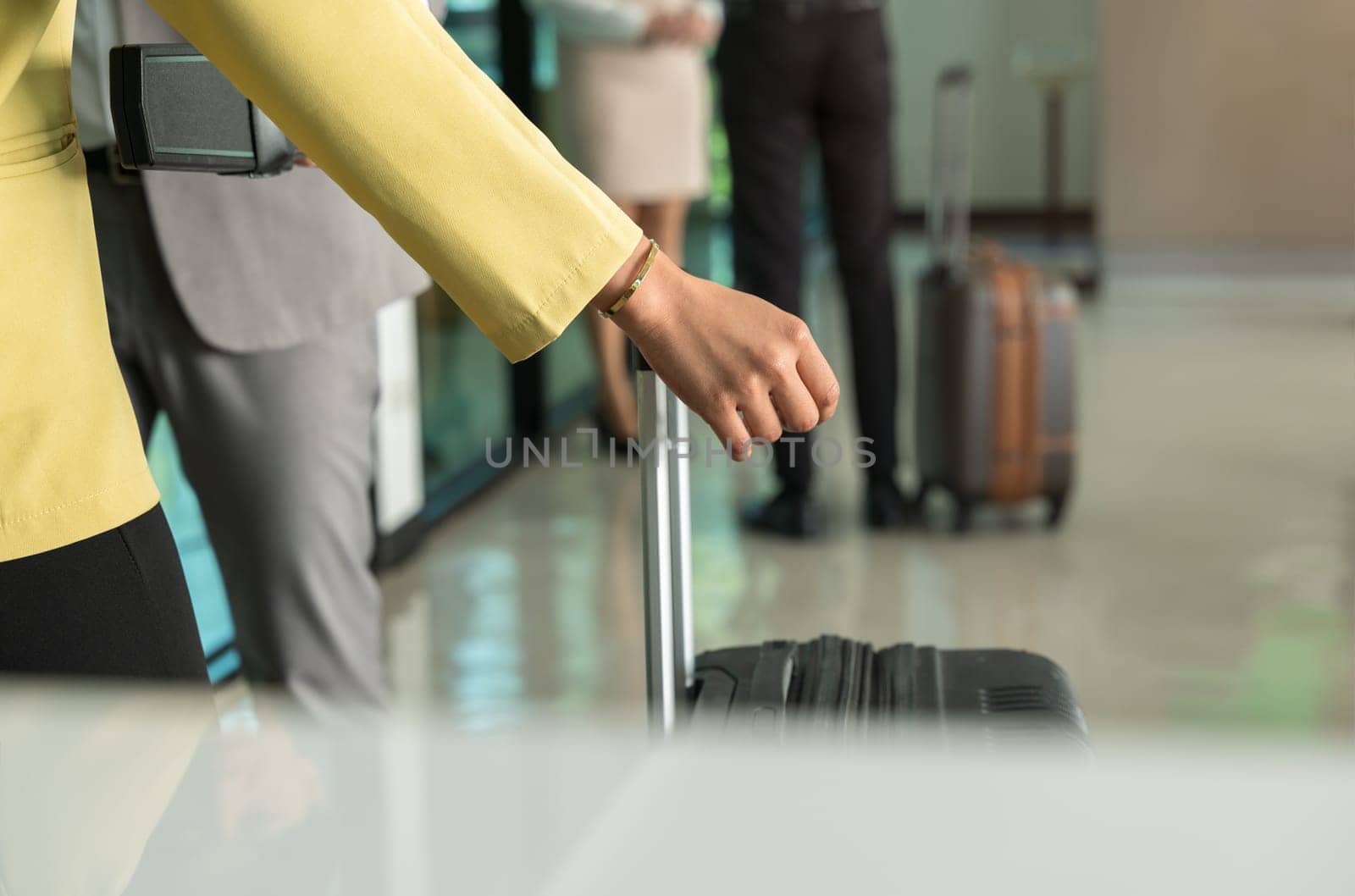 Security male officer using metal detector on female passenger in yellow jacket with suitcase at airport boarding gate. Airport travel and security concept.
