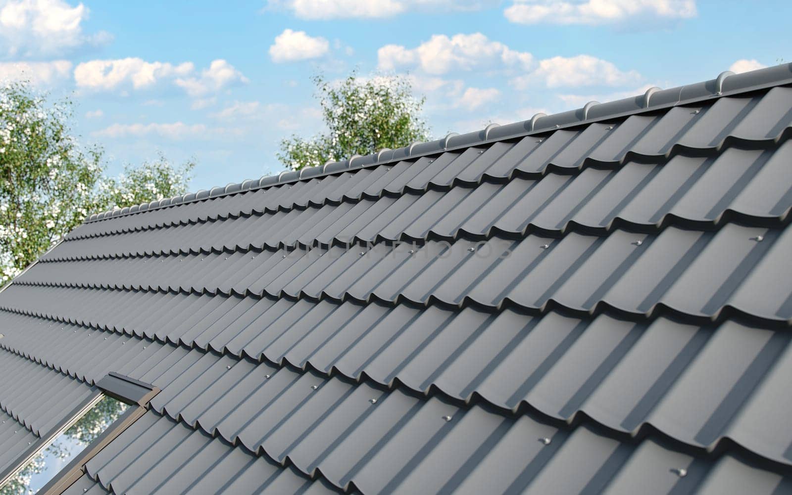 Close-up house roof with steel roofing sheet. Traditional metal shingle tiles. Gray modular tile effect roof panel. Profiled metallic corrugated pantile as clay or concrete slate. Building's covering