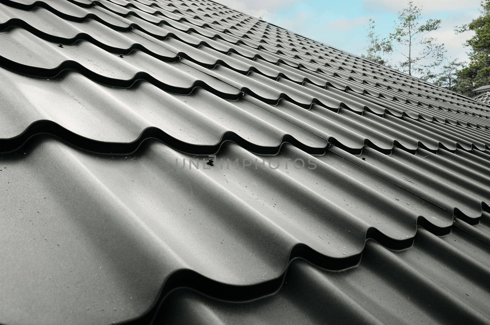 Close-up house roof with steel roofing sheet. Traditional metal shingle tiles. Gray modular tile effect roof panel. Profiled metallic corrugated pantile as clay or concrete slate. Building's covering
