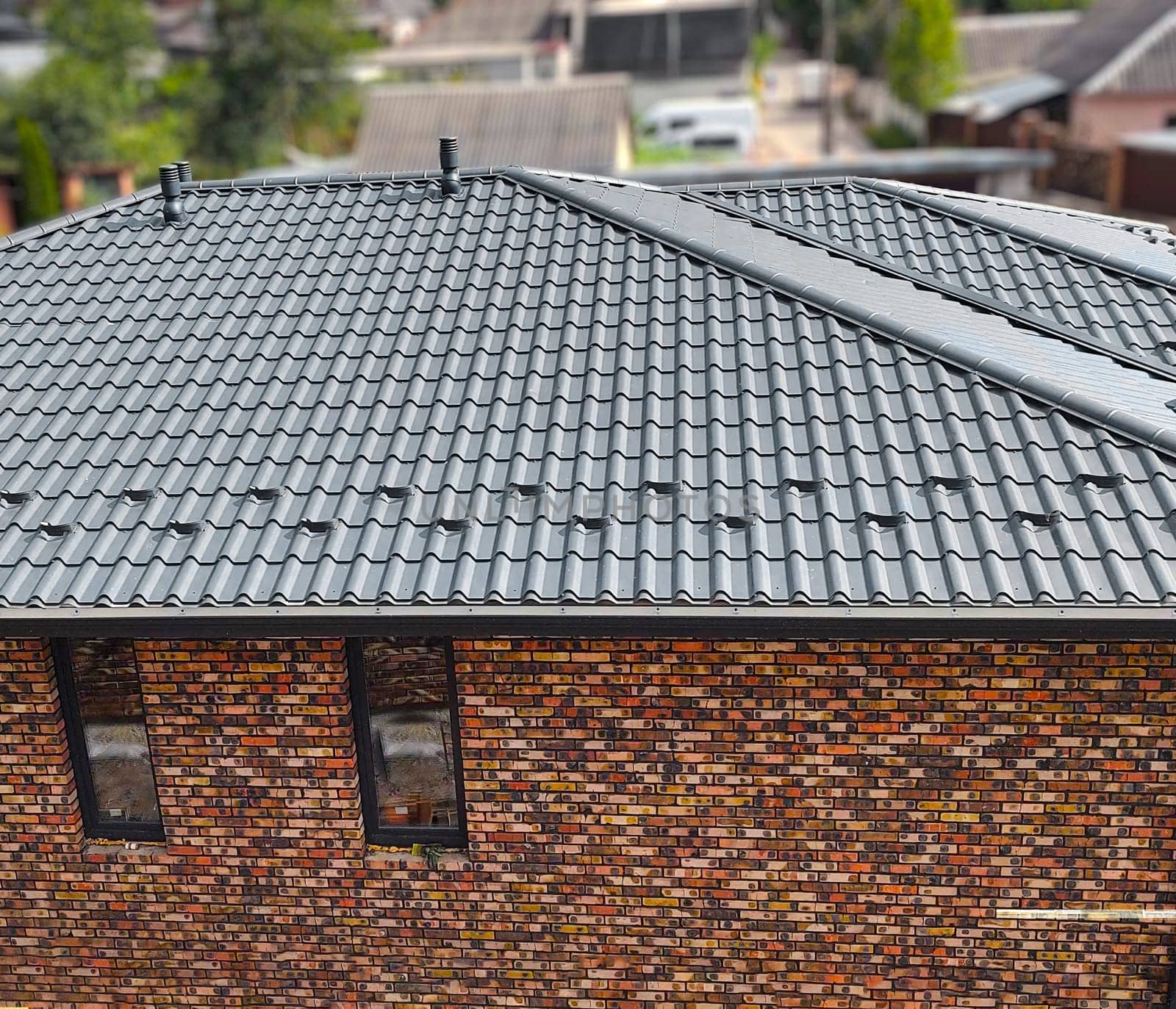 Close-up house roof with steel roofing sheet. Traditional metal shingle tiles. Gray modular tile effect roof panel. Profiled metallic corrugated pantile as clay or concrete slate. Building's covering