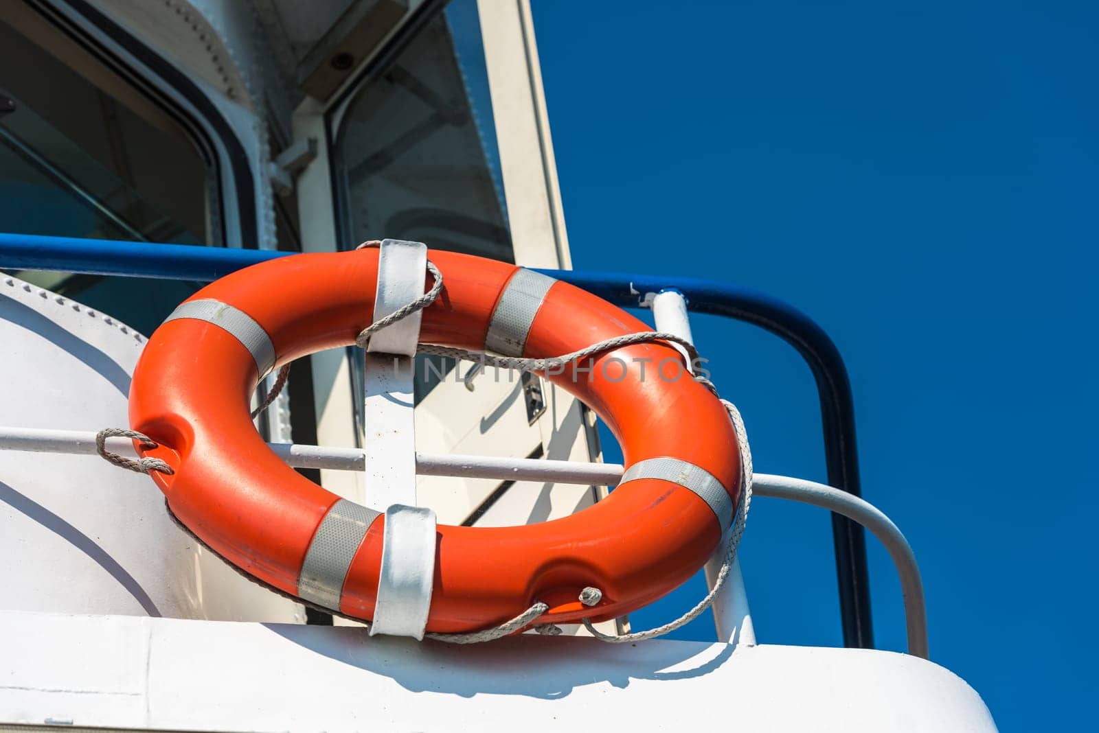 Bright orange lifebuoy on a white yacht side. Blue sky background