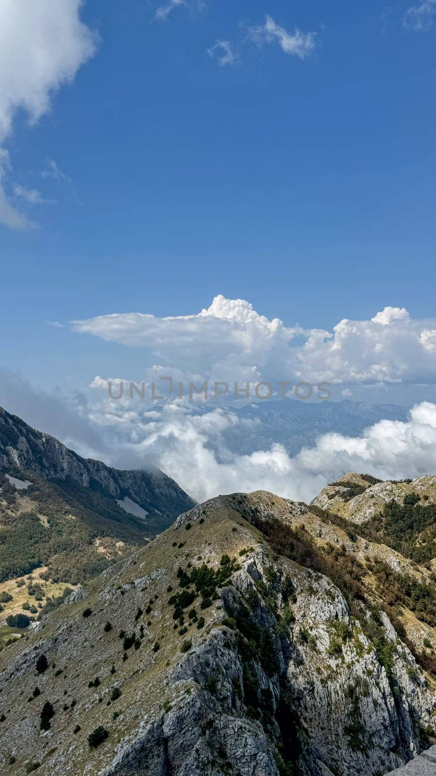 Stunning view of mountain peaks covered with lush vegetation surrounded by floating clouds and clear blue sky.
