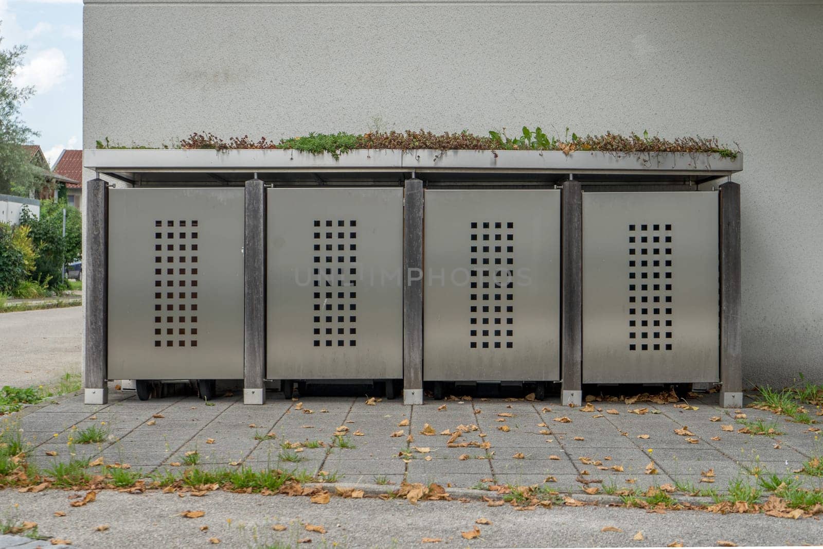 Aesthetic garbage bin with metal doors, wood and plants in front of a house wall