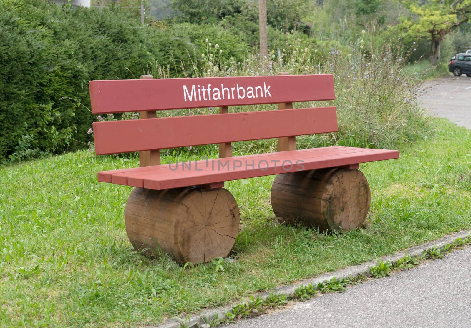 Red wooden bench on the side of the road with white writing and German text: Carpooling bench