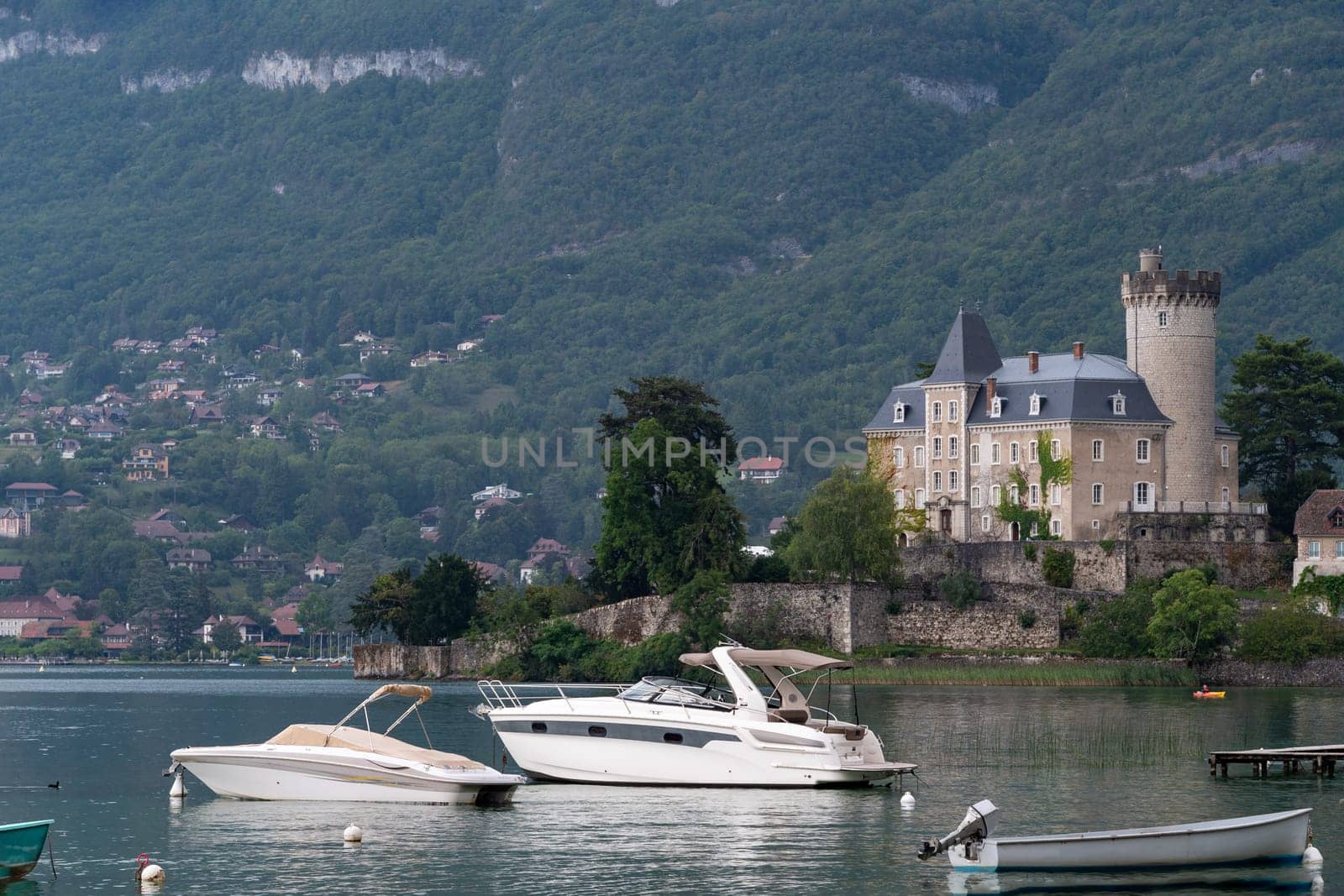 A small boat is docked next to a large boat. The water is calm and the sky is cloudy, Annecy lake