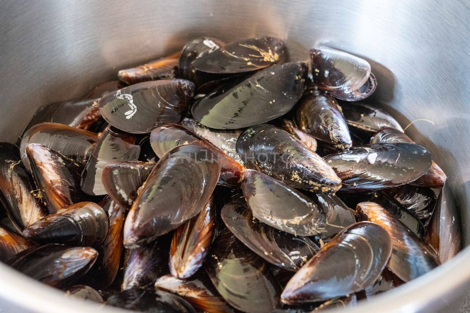 A bowl of mussels is filled with a variety of sizes and shapes. The mussels are brown and appear to be fresh. The bowl is placed on a table, and the image conveys a sense of abundance and variety