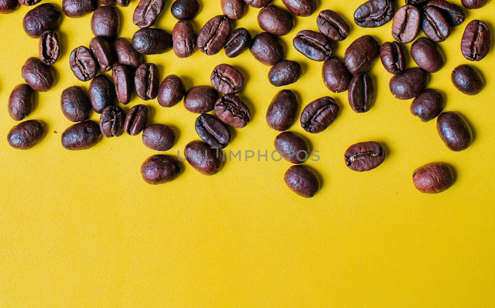 Roasted coffee beans on yellow background with copy space. Coffee grains on yellow background