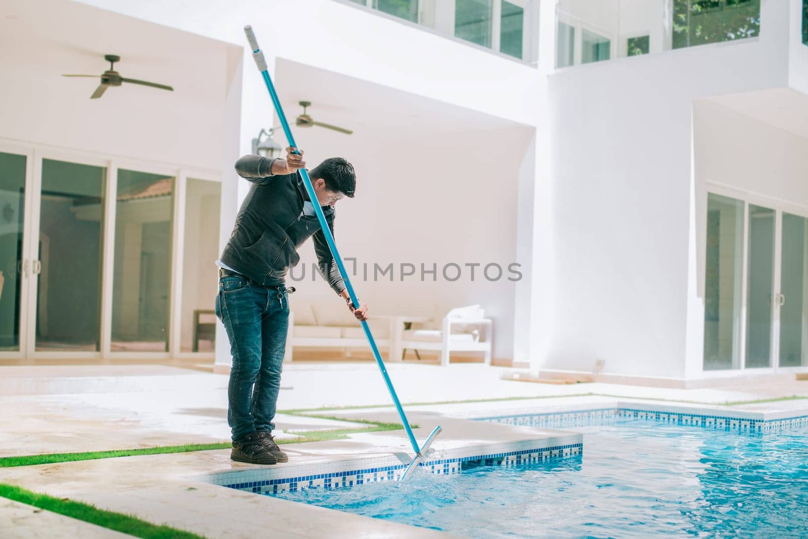 Person cleaning swimming pool with special brush. Maintenance person cleaning home pool with broom