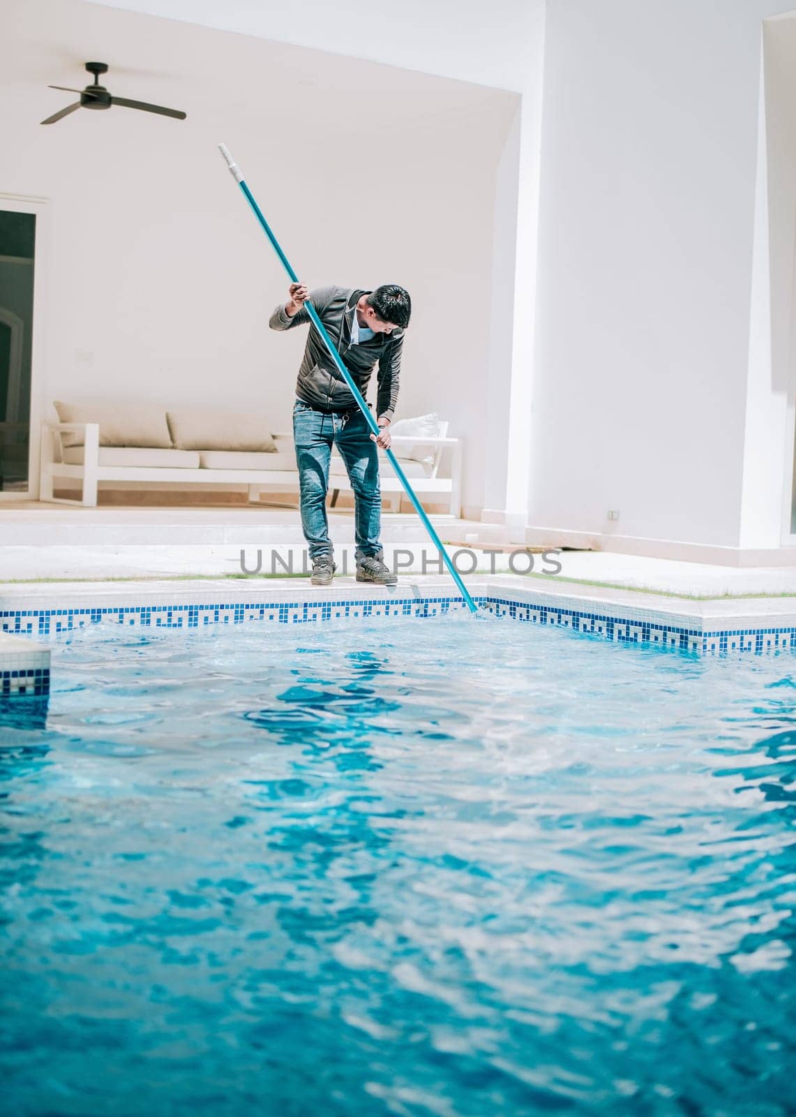 Worker cleaning a beautiful homemade swimming pool with skimmer. Maintenance person cleaning a beautiful home swimming pool