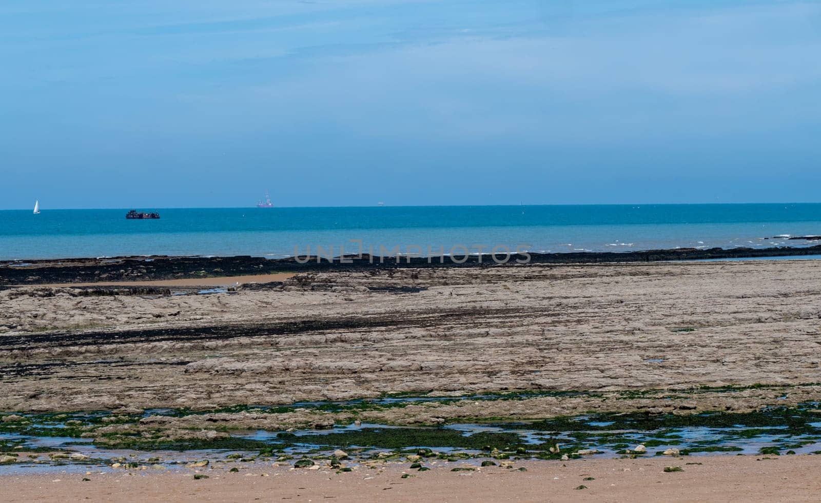 A beach with a boat in the distance and a blue sky. The sky is clear and the water is calm