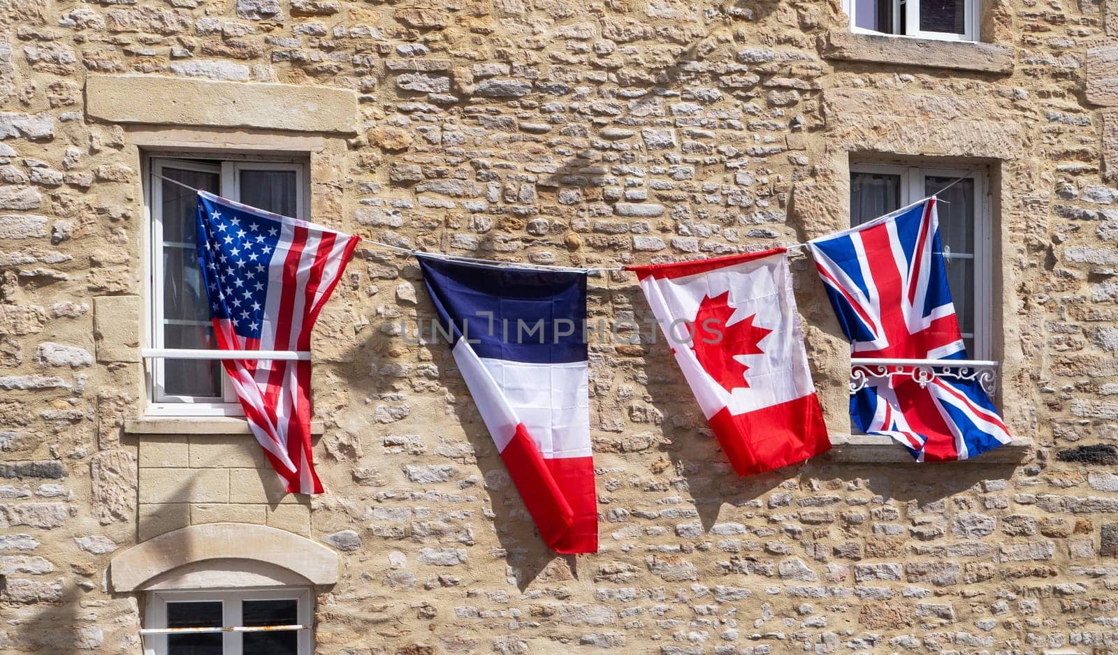 Four flags hanging from a window, including the American, British, French, and Canadian flags