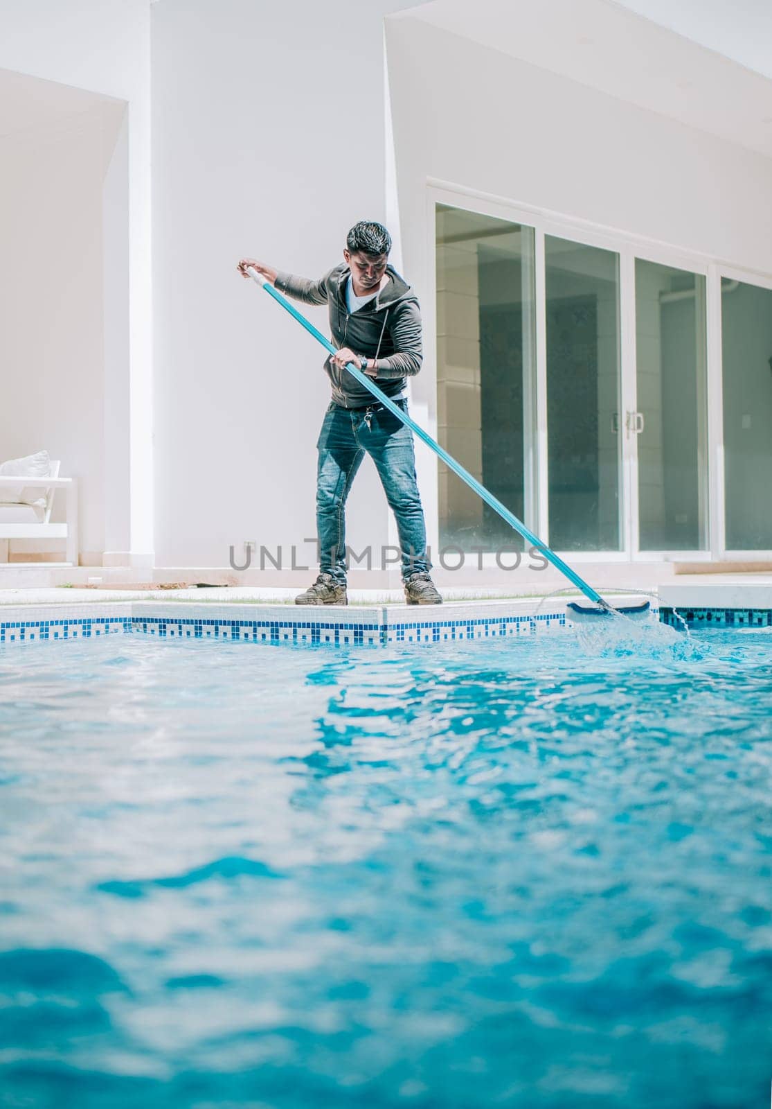 Home pool cleaning with wall brush. Male worker cleaning a home swimming pool with special brush