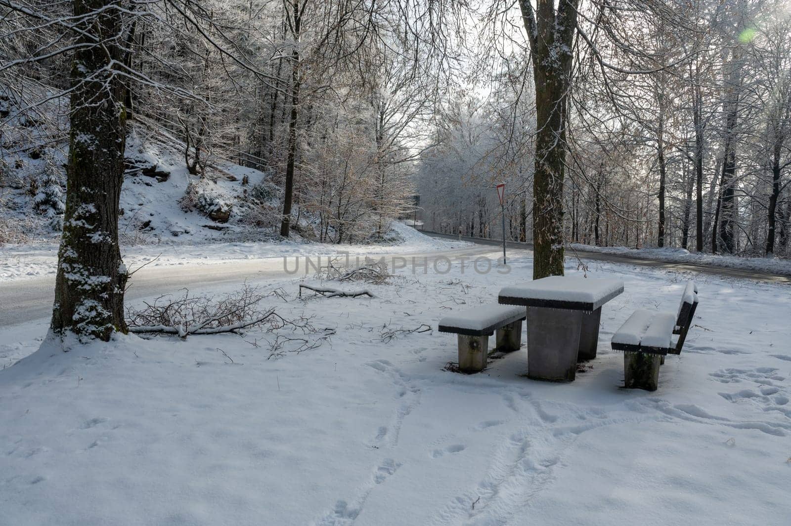 Picnic bench and table in a parking lot in the snow in a forest  with a street