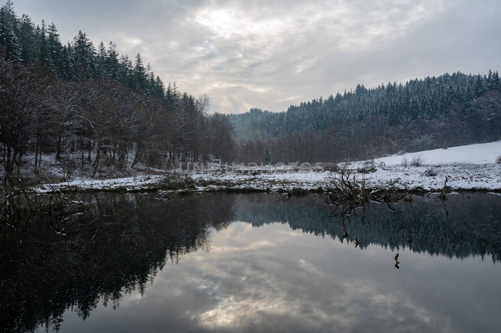 A small lake with forest and reflections in the water, in winter time with snow