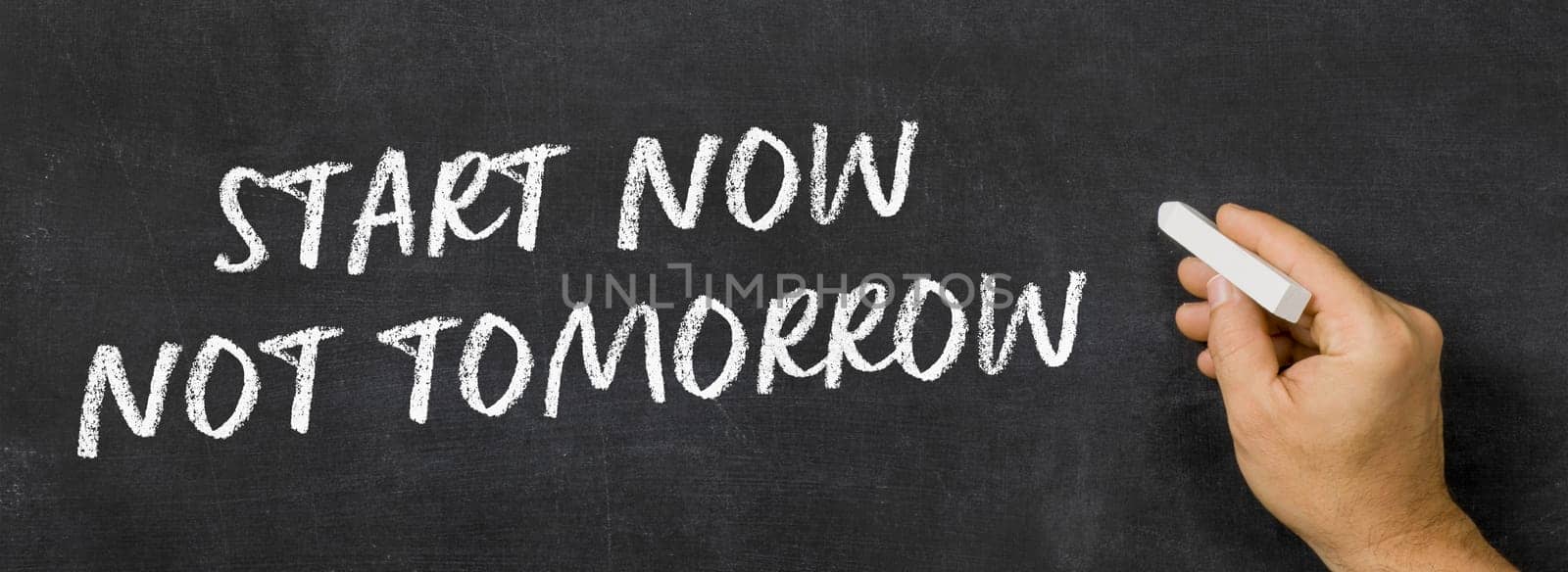 Text written on a blackboard -  Start now not tomorrow
