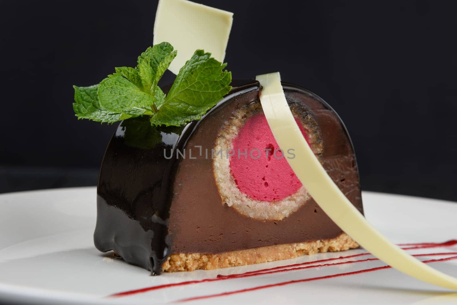 Delicious biscuit chocolate cake closeup with pink souffle decorated with mint and white chocolate on dark background
