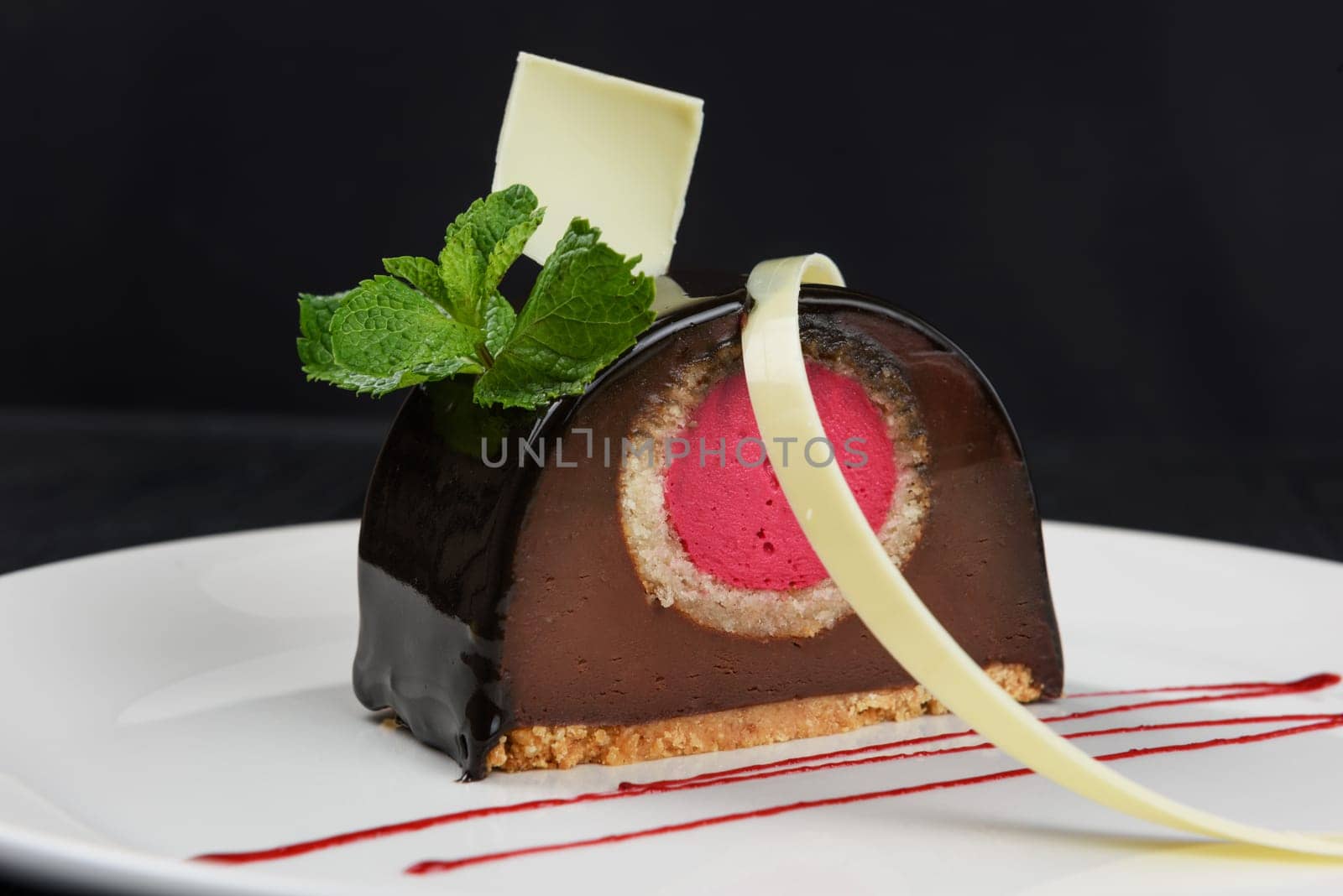 Delicious biscuit chocolate cake closeup with pink souffle decorated with mint and white chocolate on dark background