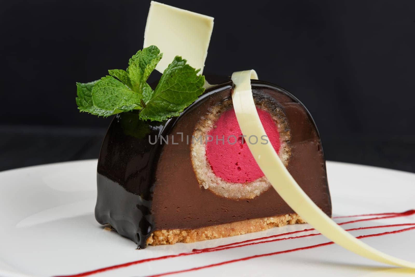 Delicious biscuit chocolate cake closeup with pink souffle decorated with mint and white chocolate on dark background