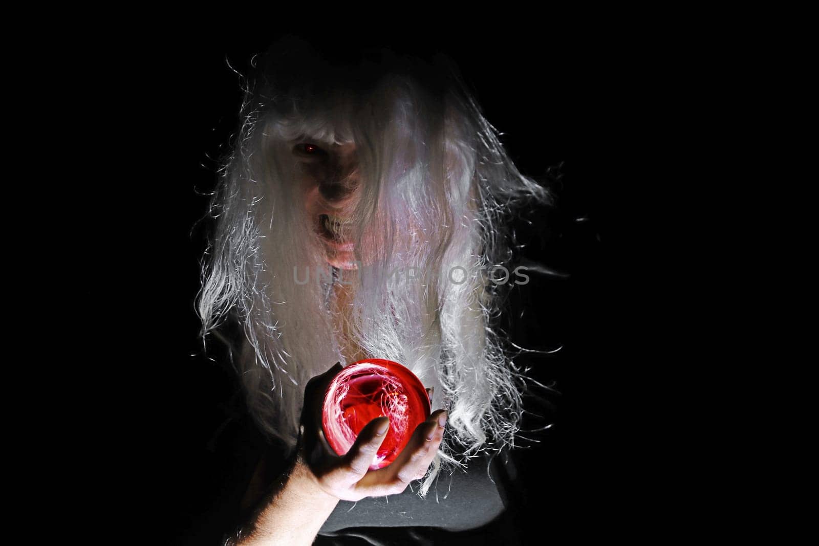 A creepy white-haired old woman with a red glass ball in the light and shadows of the night