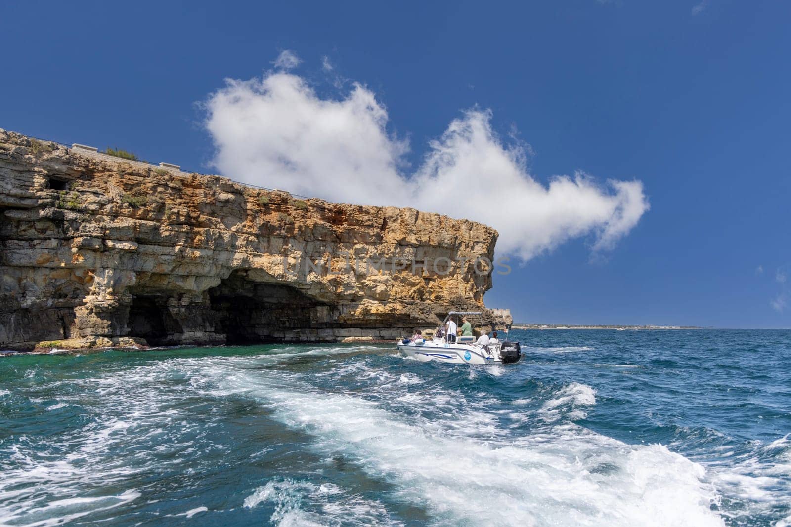 Polignano a Mare, Italy, Apulia - May 24, 2024: View from the water of picturesque cliffs by Adriatic Sea. Tourists sail by boat into a cave in the rocks
