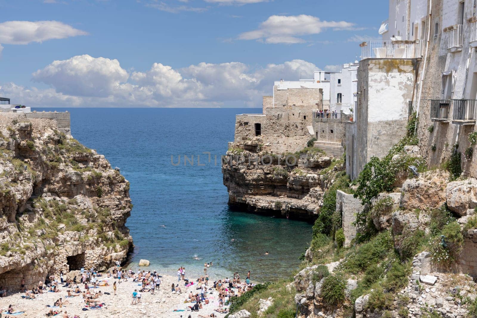 Polignano a Mare, Italy, Apulia - May 24, 2024: Lama Monachile beach, located between picturesque cliffs by Adriatic Sea. People relaxing on stone shore and swimming in the water