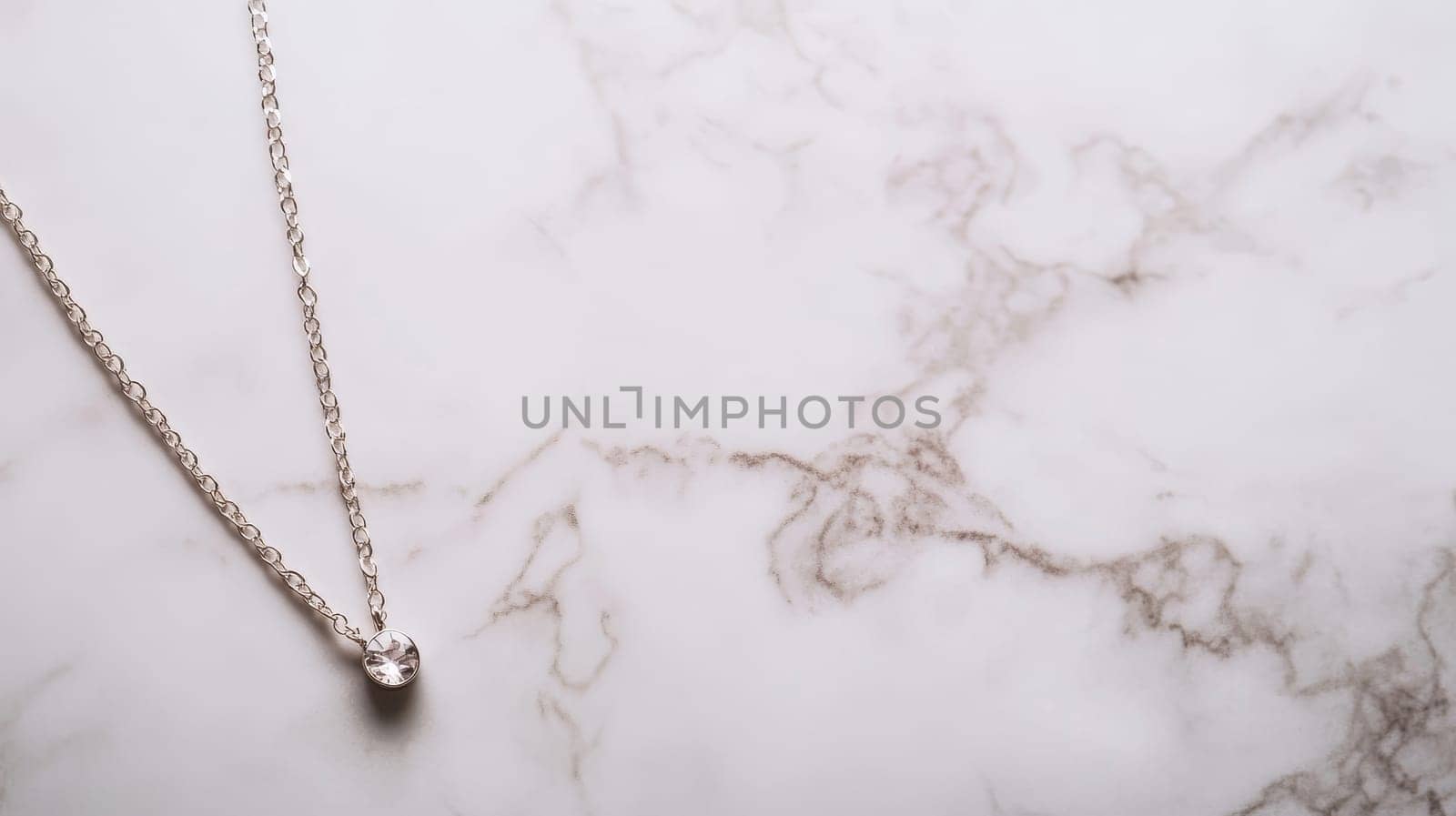 Elegant silver necklace with a small pendant on a white marble background, perfect for jewelry photography or product showcase.