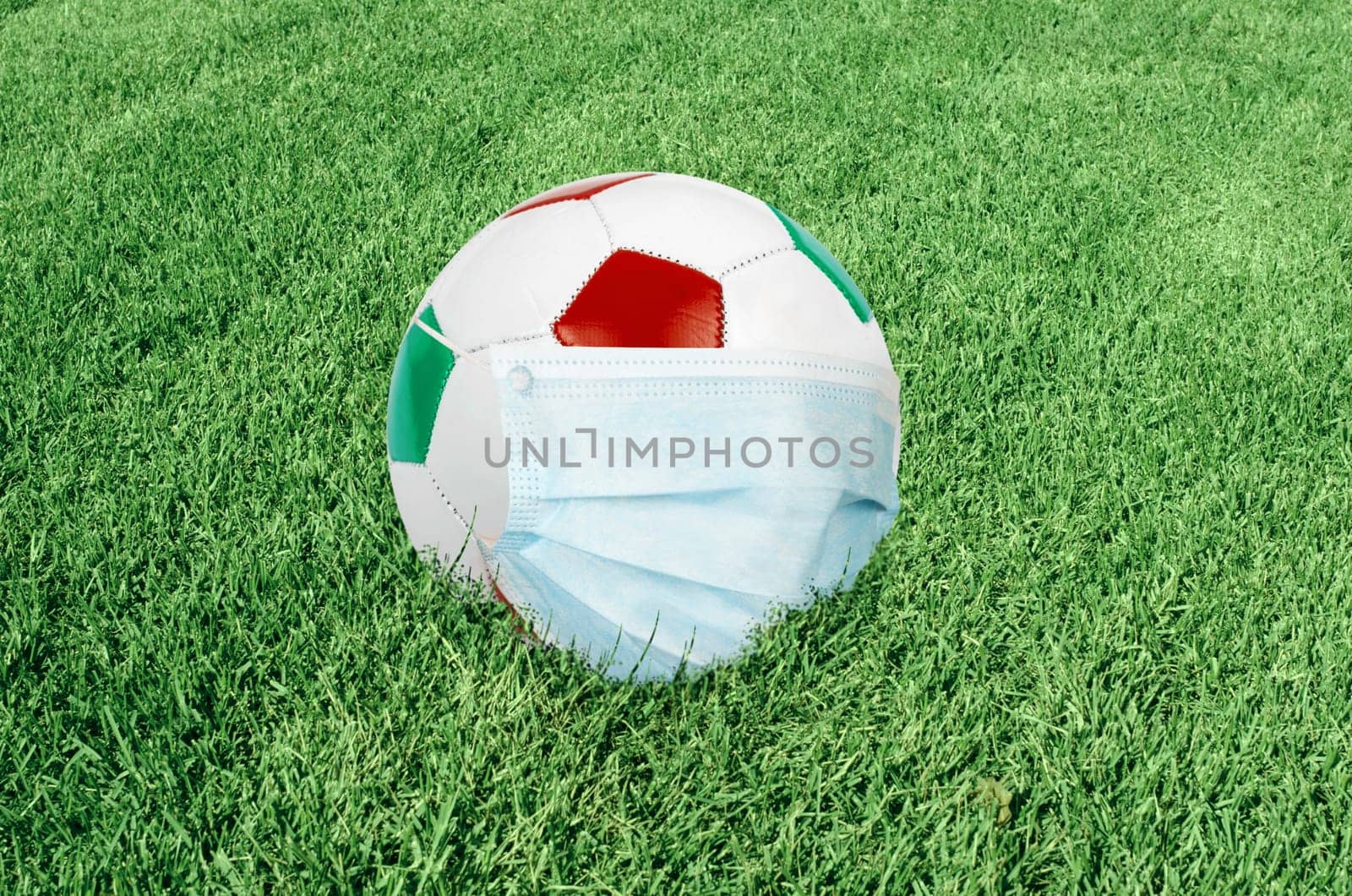 Soccer ball in italian colors with mask on green field. Virus threatened championship concept