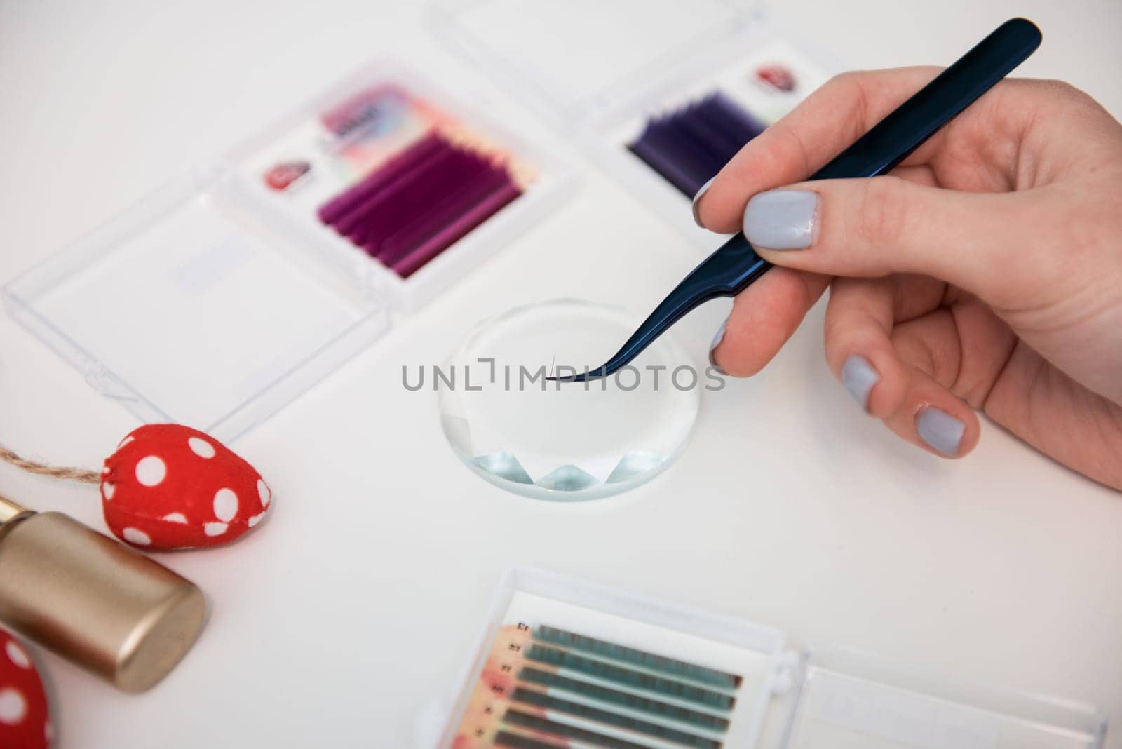 Tools for eyelash extension procedure. Hand with tweezers with artificial black lashes on gray background. Beauty concept