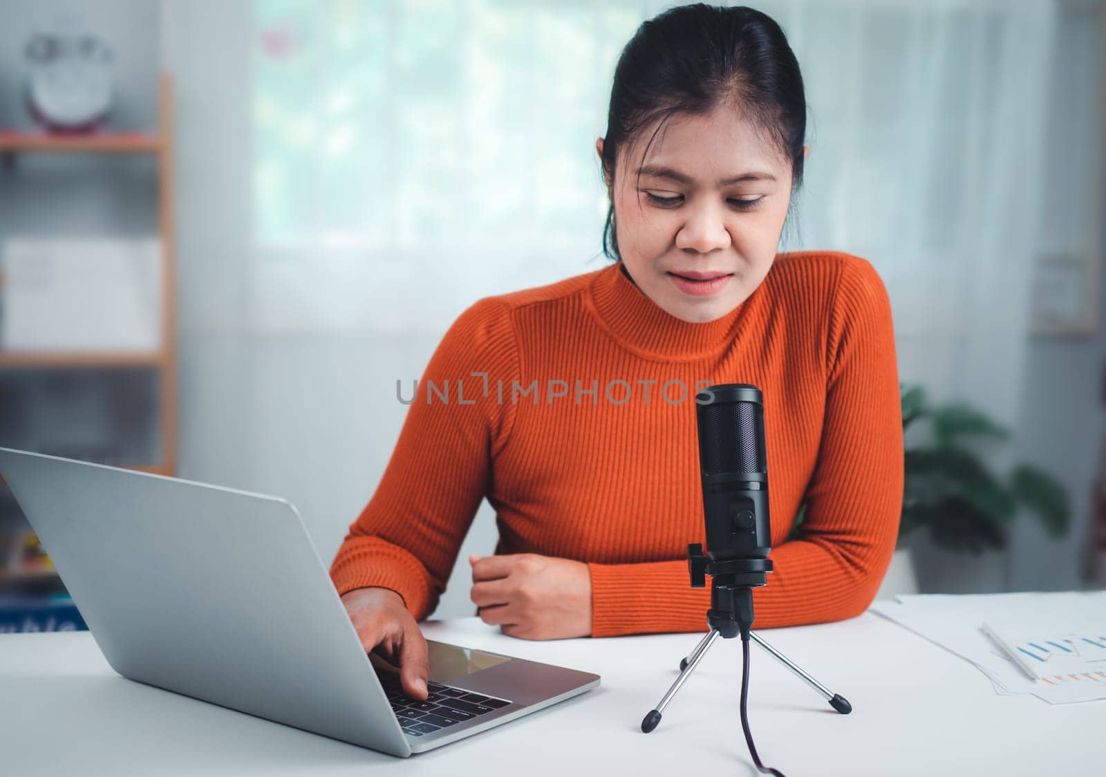 Woman talking into microphone on stand, lead on-line communication, discuss topic, looks at notebook screen, engaged in streaming, virtual meeting event, Podcast, webinar, Content creator concept.