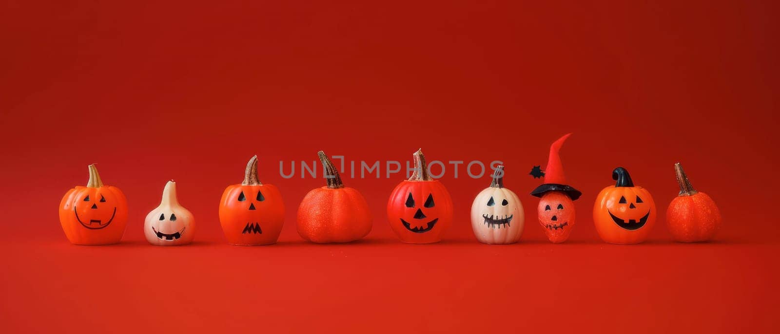 A set of creatively painted pumpkins and gourds is lined up against a vibrant red backdrop, showcasing various Halloween-themed expressions and decorations, adding a festive touch to the season.