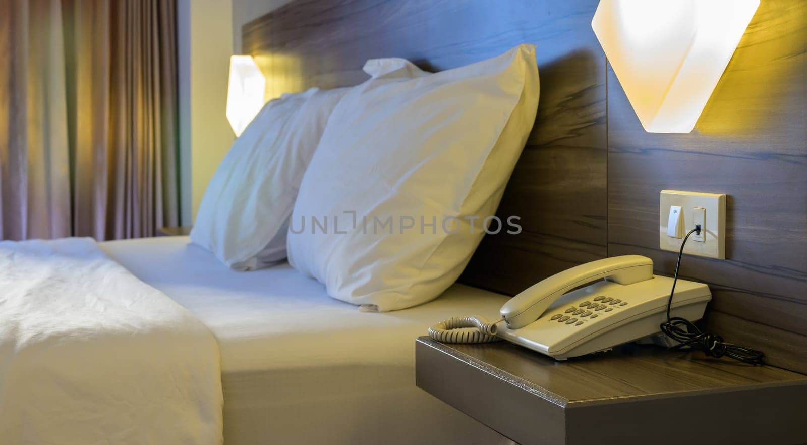 Simply furnished hotel room with white bed, pillows, telephone and lamp