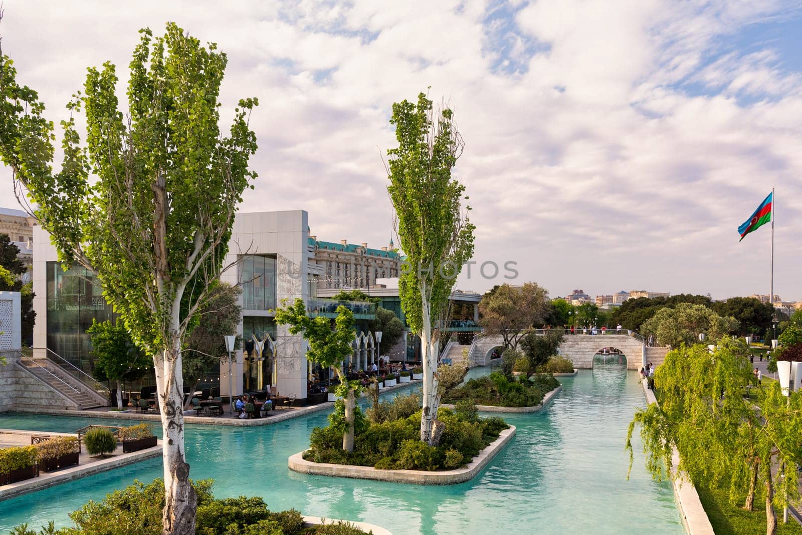 Baku, Azerbaijan - May 4 2024: The Boulevard canals, or Little Venice, surrounded by lush greenery, and Azerbaijani flag in distance
