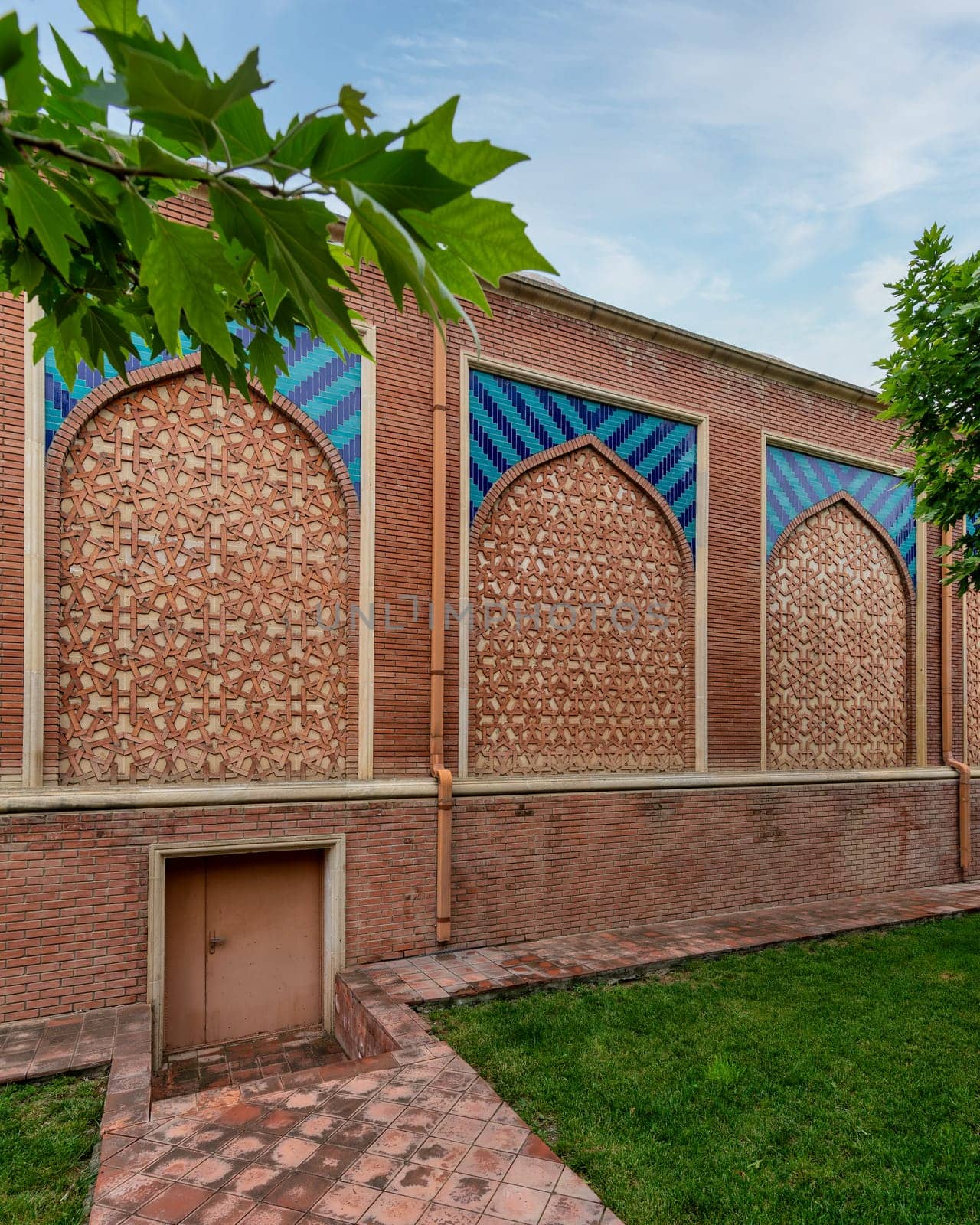 A traditional brick wall adorned with intricate geometric patterns and colorful tiles stands in a well-maintained garden, showcasing architectural beauty and harmony with nature