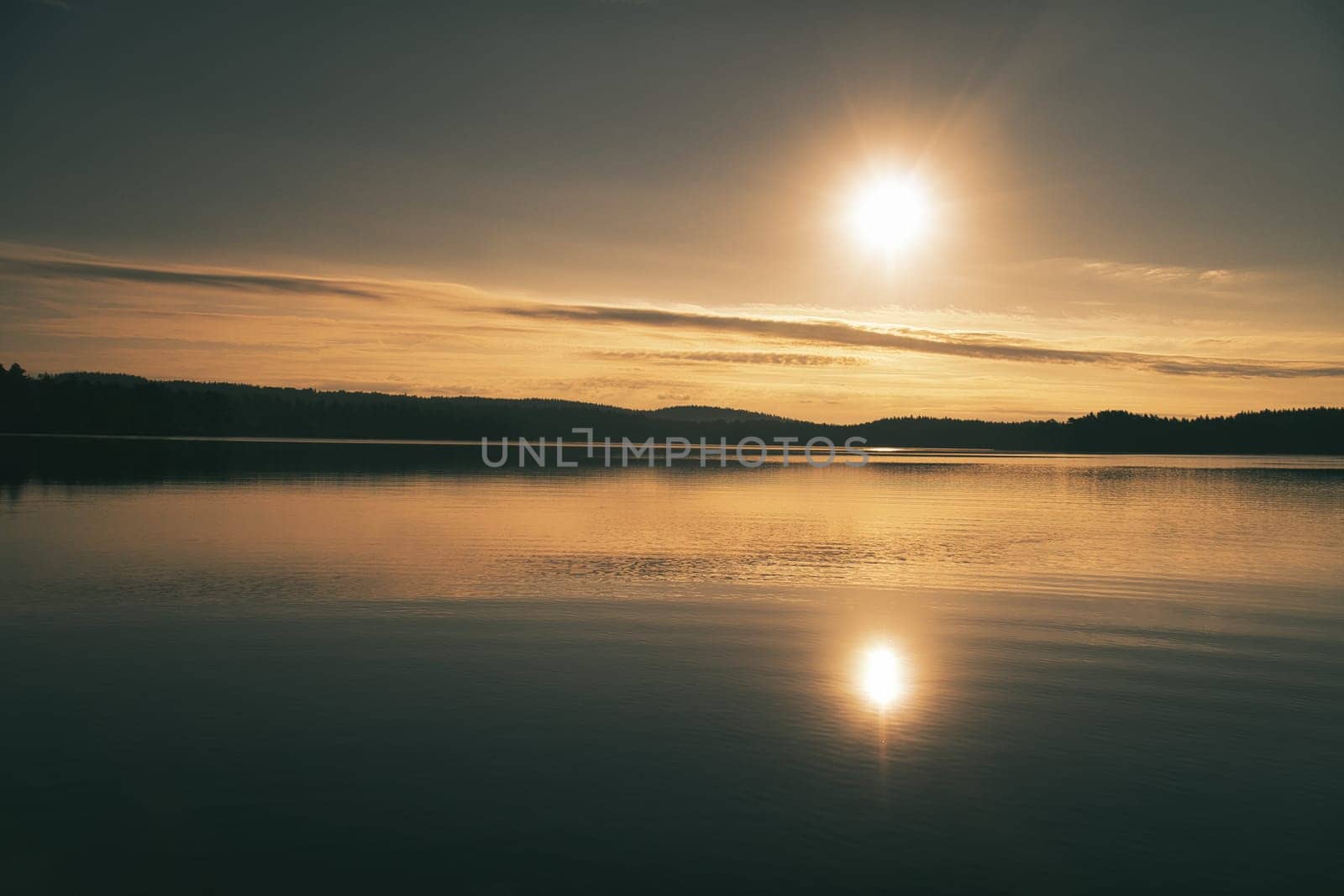 Sunrise over a Swedish lake with mirror-smooth water in front of trees on the shore. Nature shot from Scandinavia