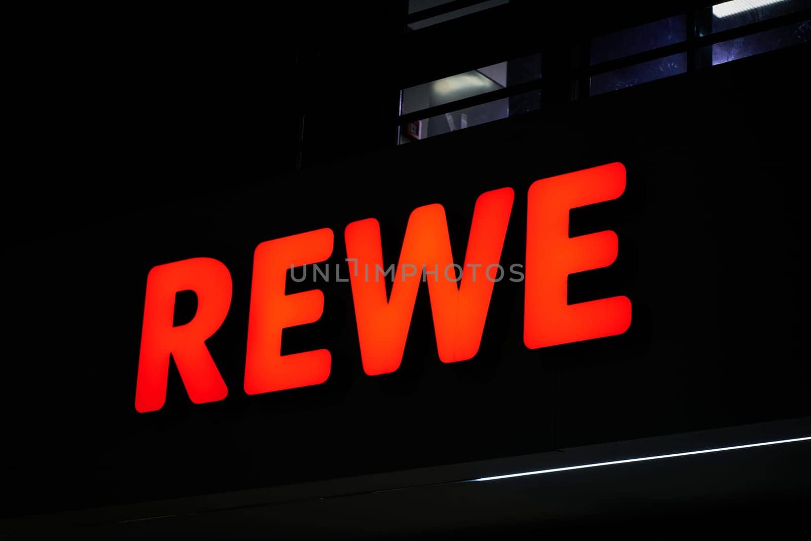Illuminated advertisement of the German food retailer Rewe at a Rewe supermarket in the evening in Berlin