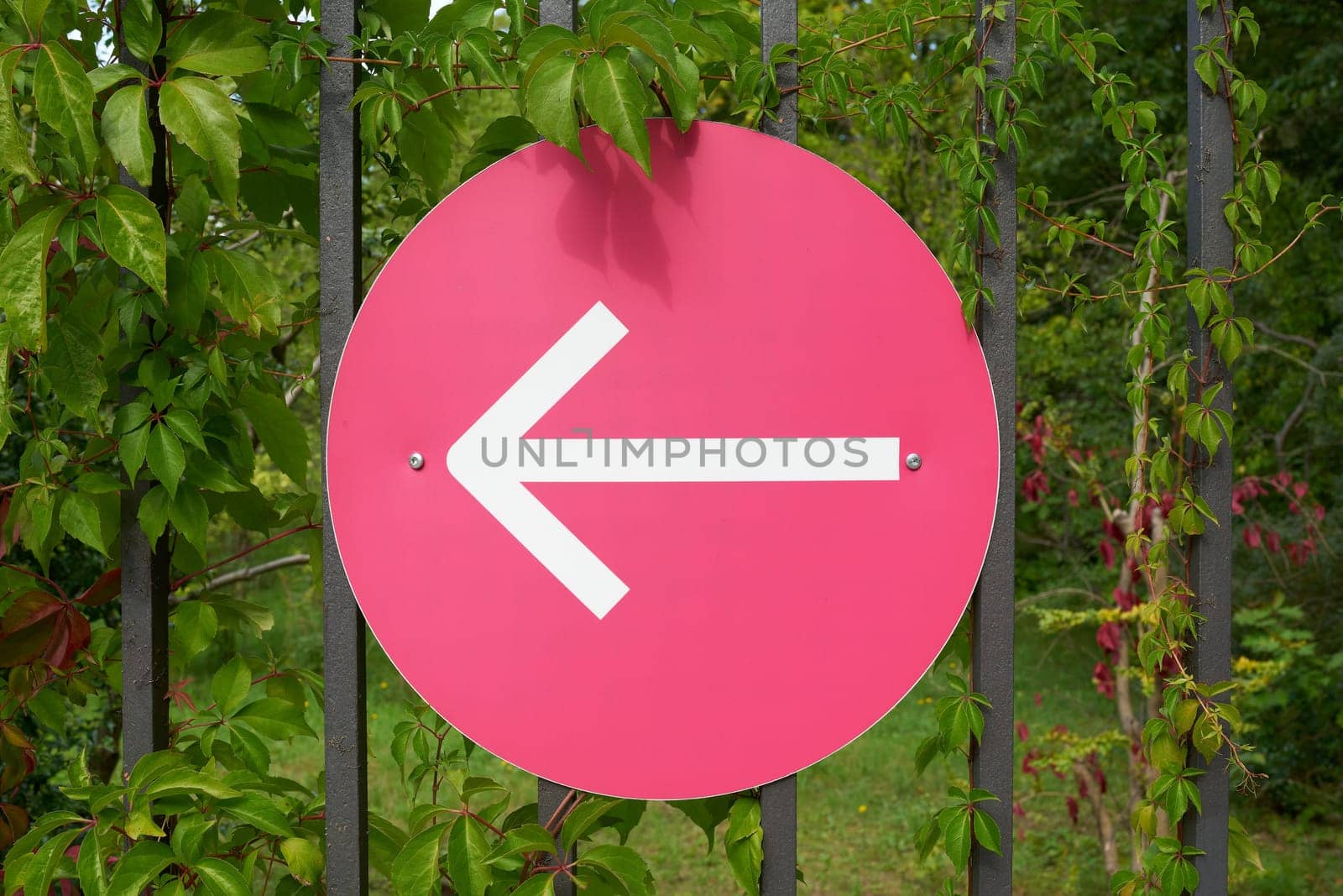 Sign with an arrow pointing left on a fence, indicating the right direction