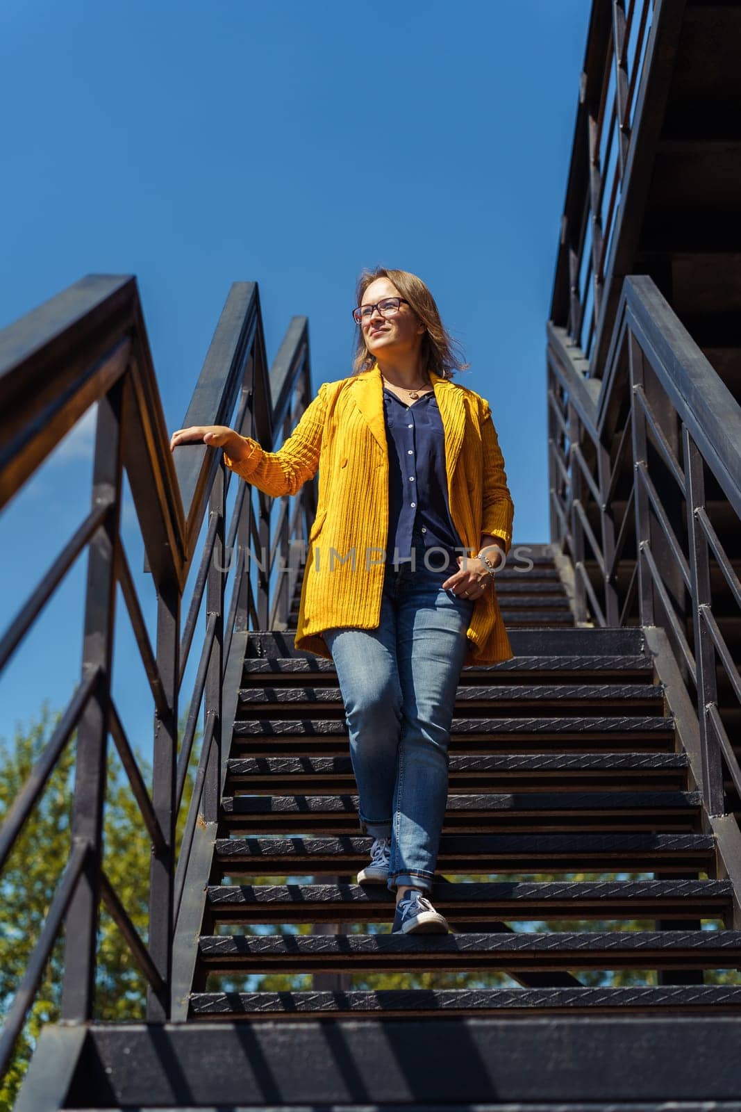 Middle-aged woman descending an outdoor staircase with one hand on the railing.