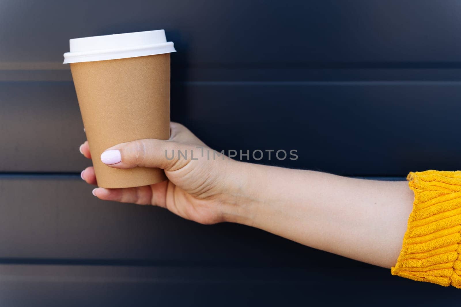 Hand holding disposable coffee cup on blue background.