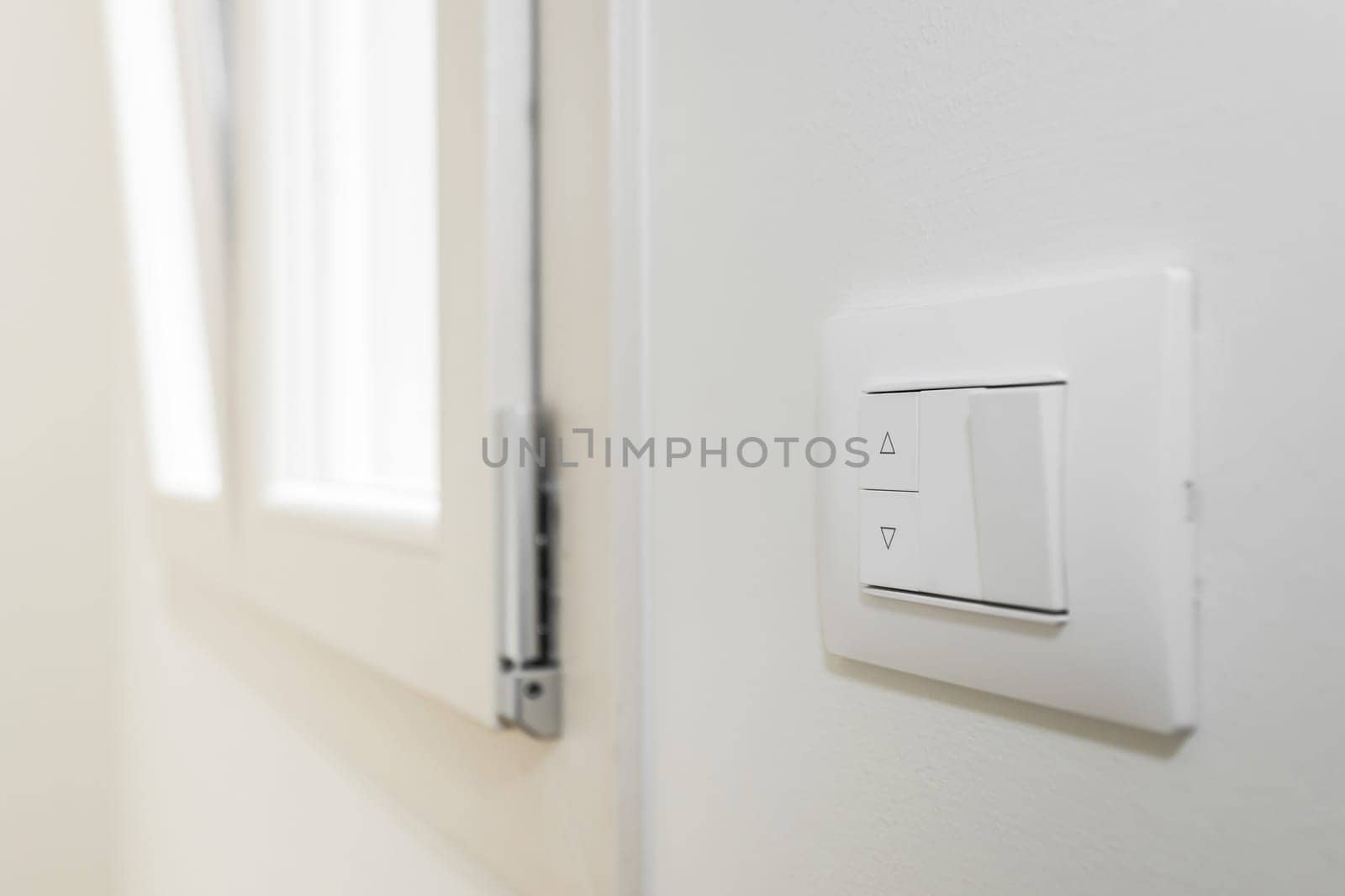 White frame and buttons of the roller shutter switch up and down on white wall in the house