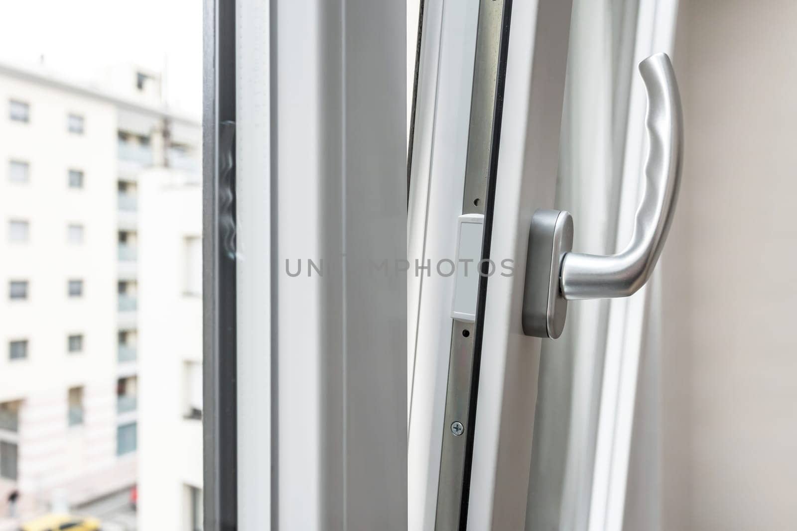 Aluminum window open detail. Bottom hung window. Metal, PVC door frame closeup view. Stylish chrome handle. Energy efficient and safety profile. Urban blurred background.