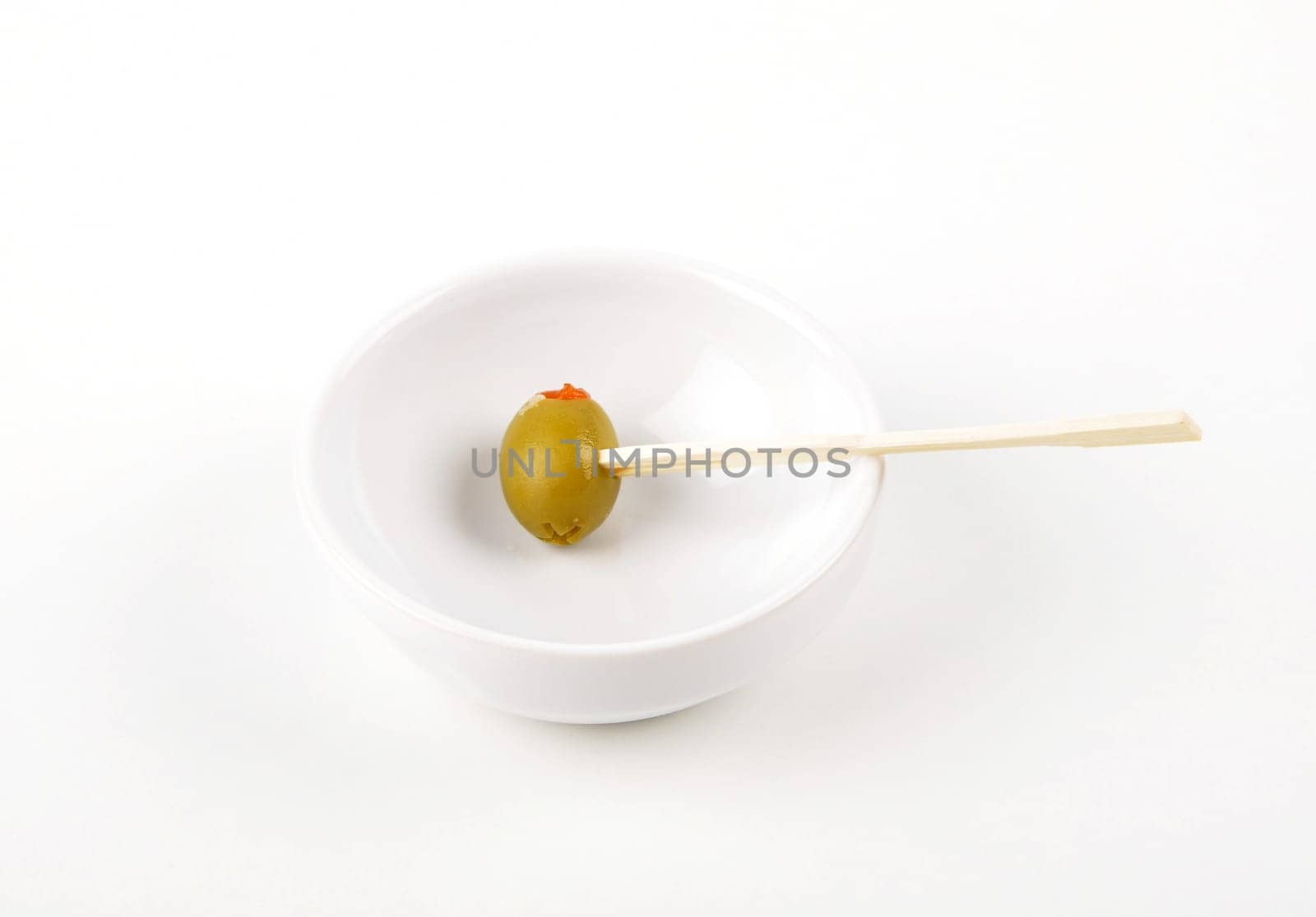 Olive with paprika on wooden skewer in porcelain bowl on white background