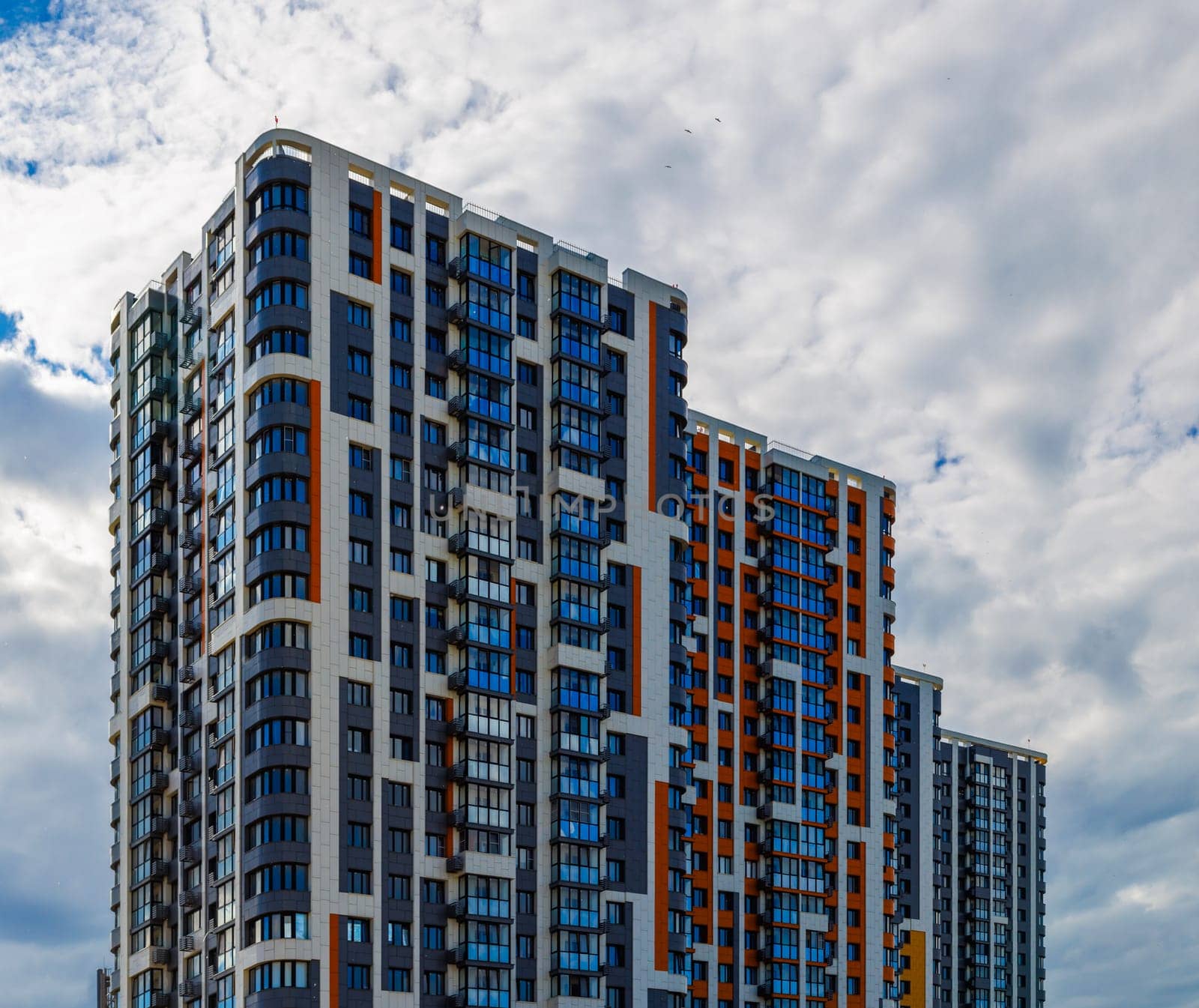 freshly built high rise apartment building on blue sky background with white clouds.