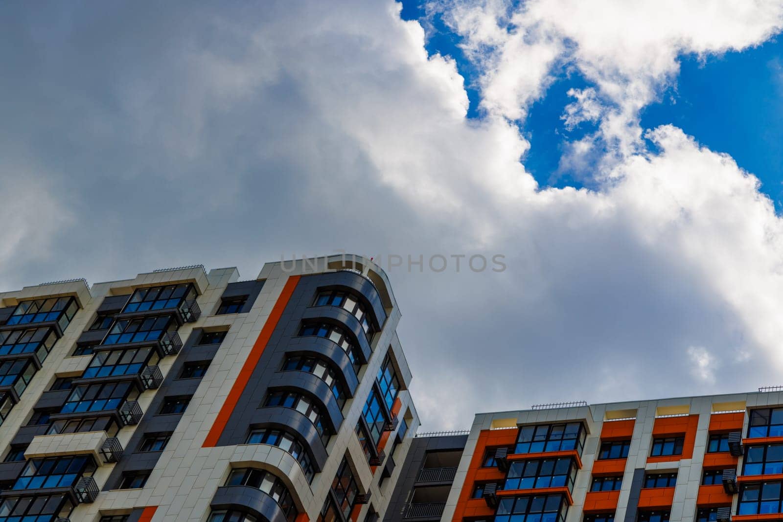 freshly built high rise apartment building on blue sky background with white clouds.