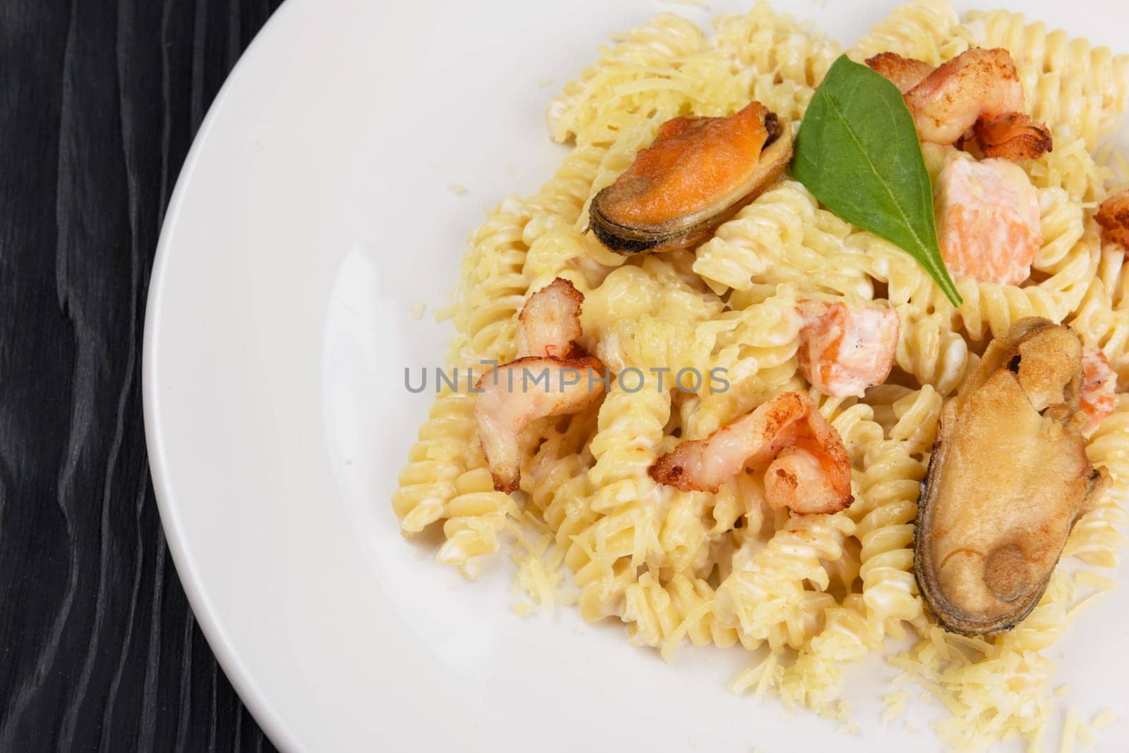 Seafood Pasta with mussels salmon and shrimps with basil in white plate on black wooden background.
