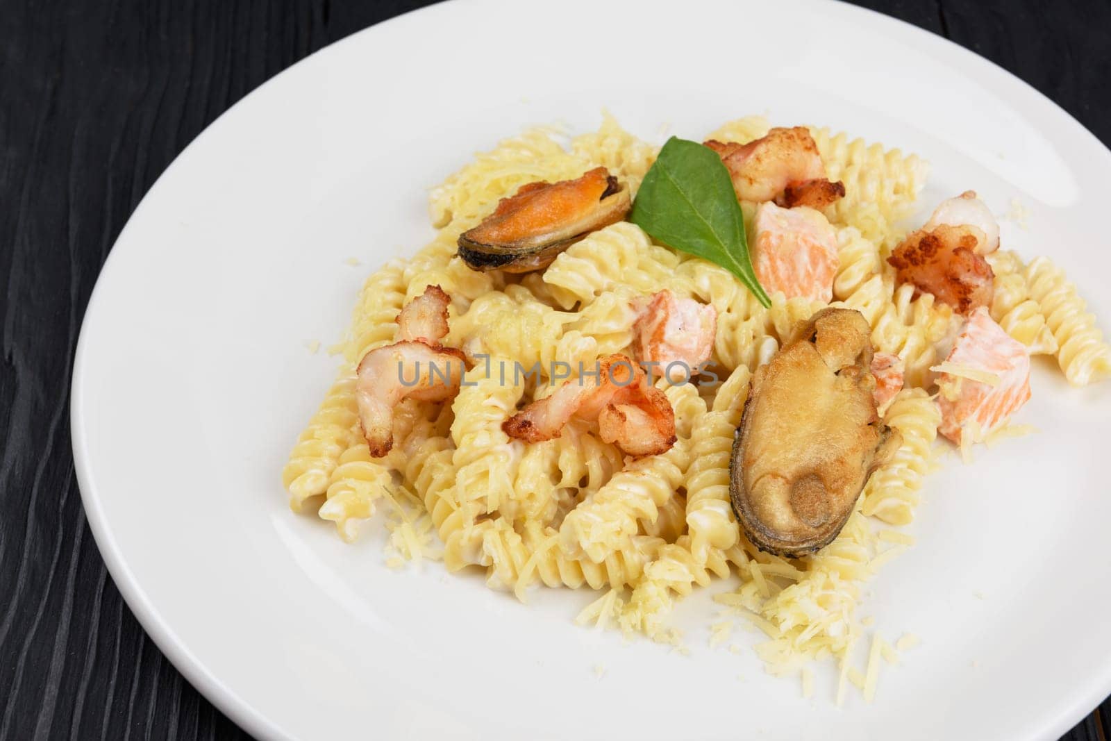 Seafood Pasta with mussels salmon and shrimps with basil in white plate on black wooden background.