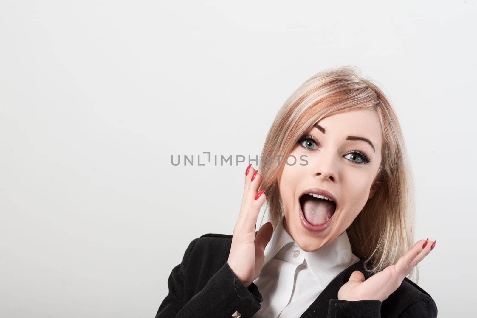 Shocked, excited businesswoman in a suit jacket stands against a white background, exuding joy and amazement with wide eyes and open mouth