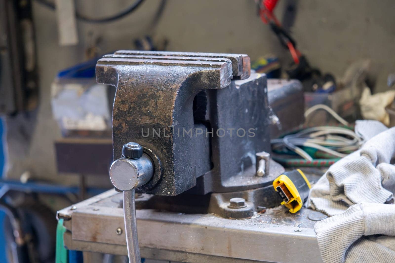 A black and silver tool with a yellow handle sits on a table. The tool is a vise, and it is in a workshop setting