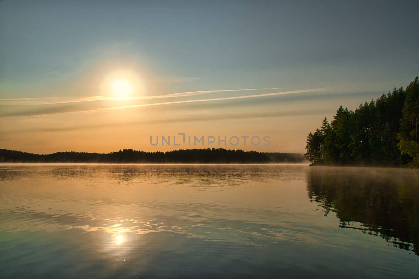 Sunrise over a Swedish lake with mirror-smooth water in front of trees on the shore. Nature shot from Scandinavia