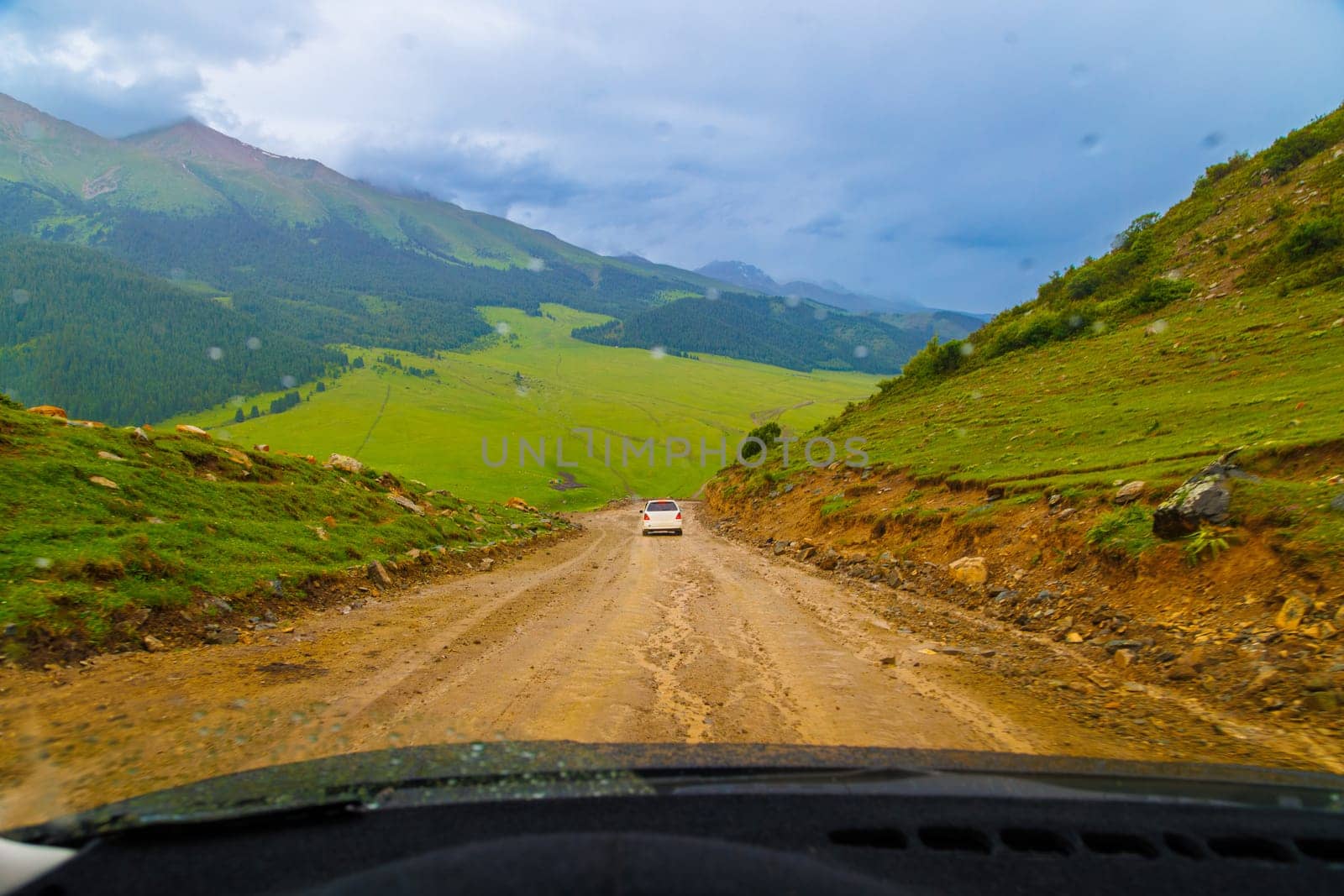 cars driving down the dirt road at rainy summer day in mountains, view from drivers perspective.